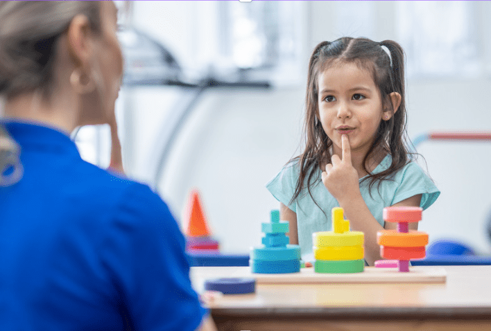 A girl pointing to her mouth while talking to a speech pathologist